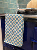 Blue kitchen towel with white floral pattern hanging on a stove handle.